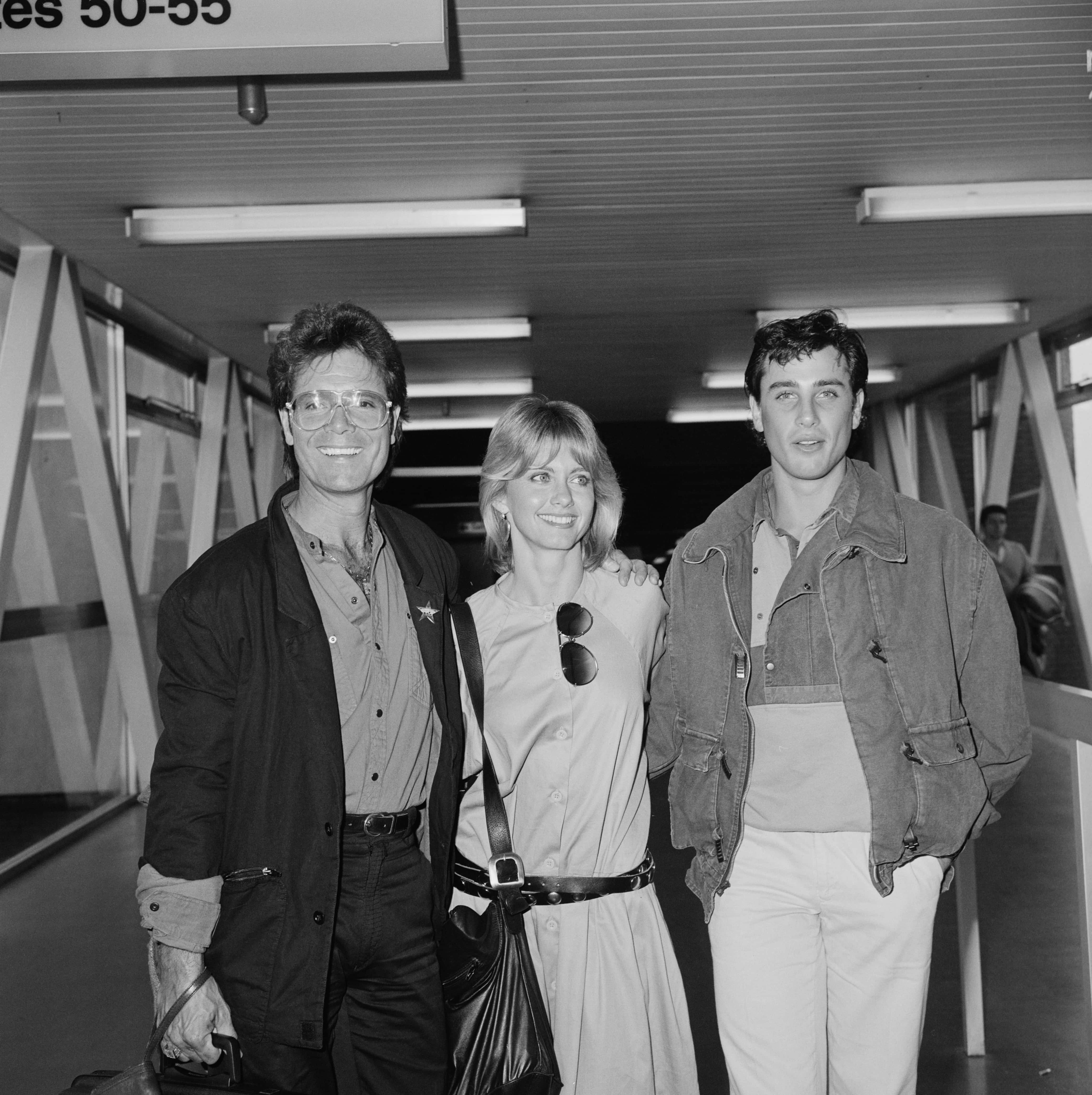 British singer, musician and actor Cliff Richard, English-Australian singer-songwriter and actress Olivia Newton-John, and American actor and dancer Matt Lattanzi at Heathrow Airport, LOndon, UK, 25th September 1983. (Photo by Parker/Daily Express/Hulton Archive/Getty Images)
