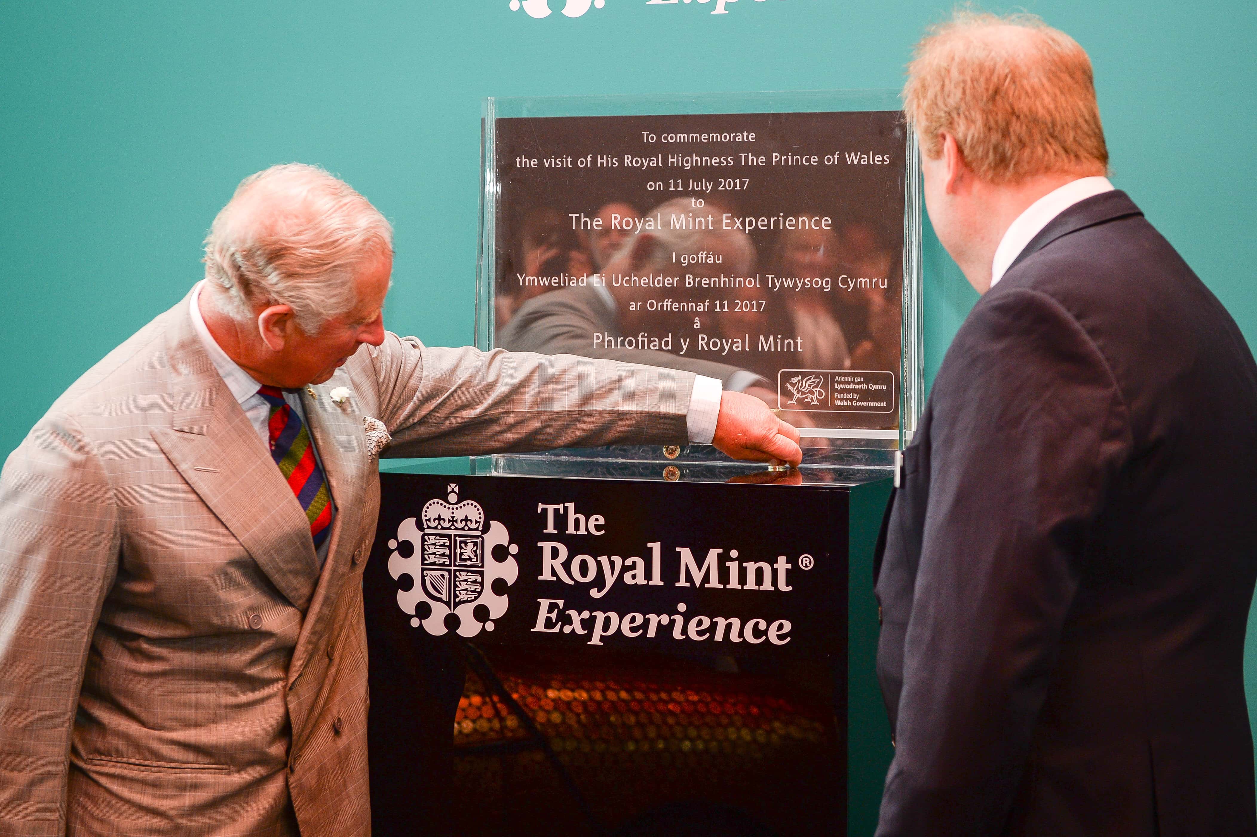 Prince Charles, The Prince of Wales  picks up a scattered pound coin after unveiling a plaque with Royal Mint CEO Adam Lawrence (right), during a tour of The Royal Mint's visitor centre  on July 11, 2017 in Heol-Y-Sarn, Wales.