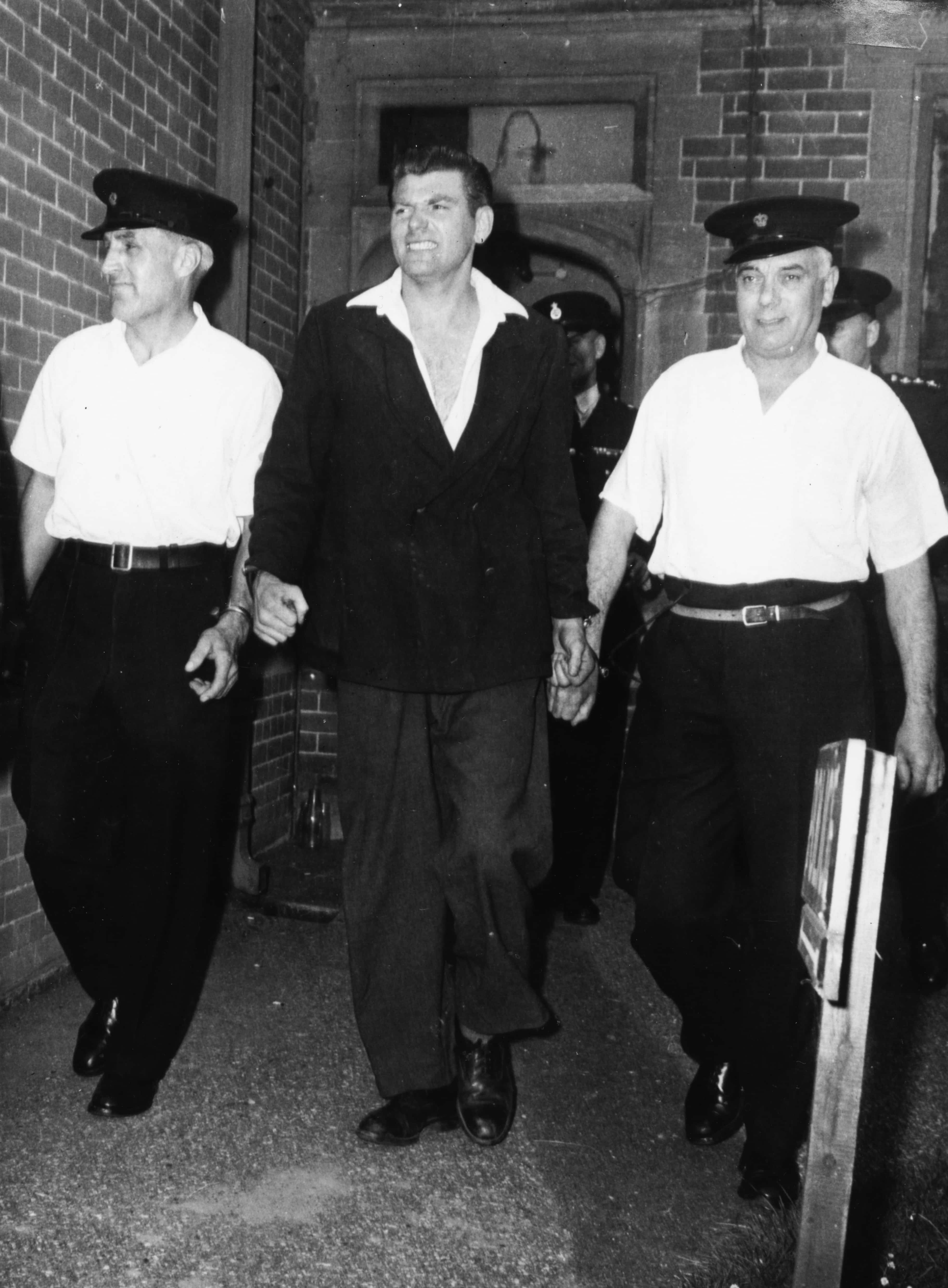 English criminal Frank Mitchell, or 'The Mad Axeman', flanked by two prison guards prior, following his recapture after he escaped from Broadmoor Hospital, 1958. Printed following a more recent prison escape from Dartmoor on December 15th 1966. (Photo by Keystone/Hulton Archive/Getty Images)