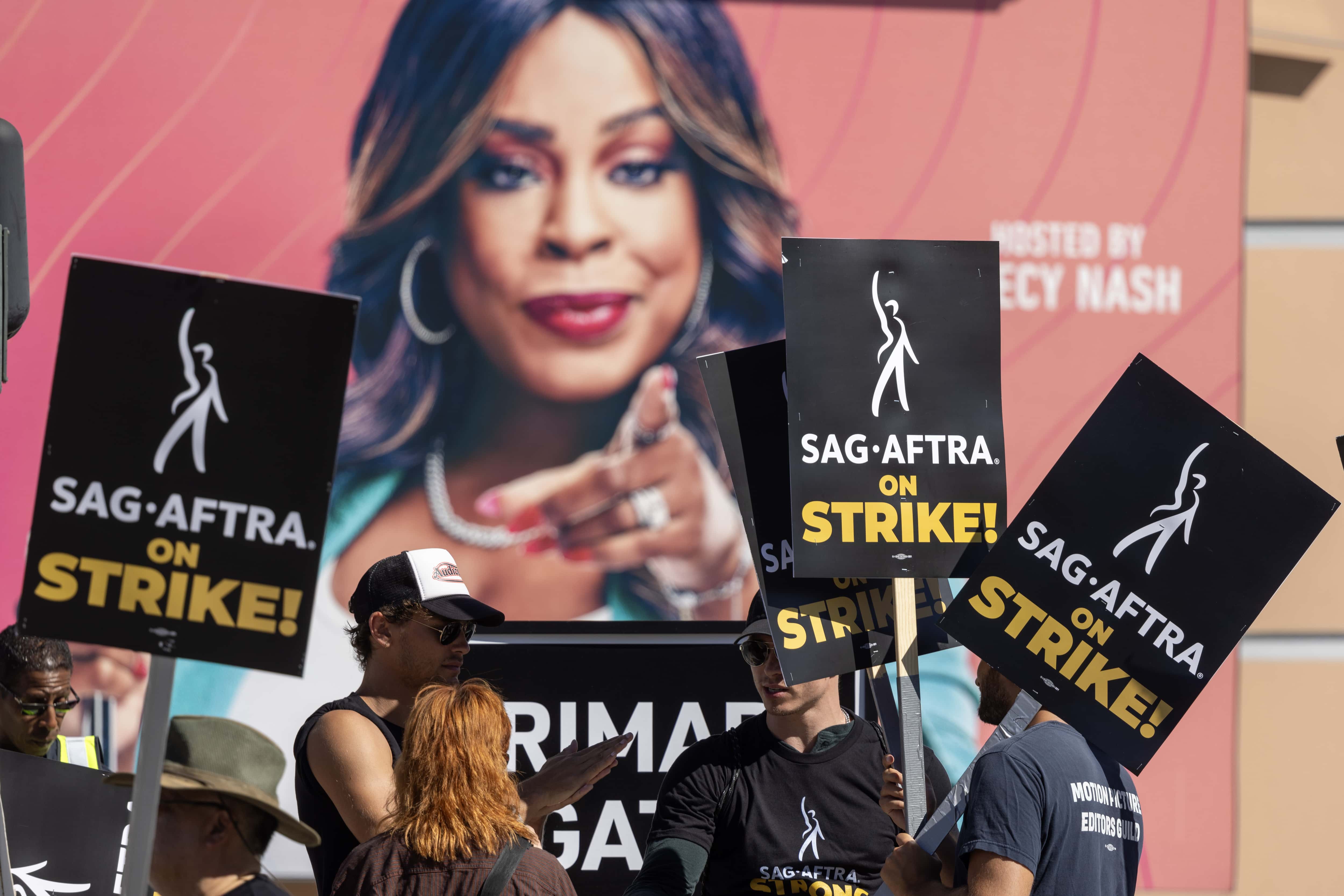 Members of the Hollywood actors SAG-AFTRA union walk a picket line near an image of 