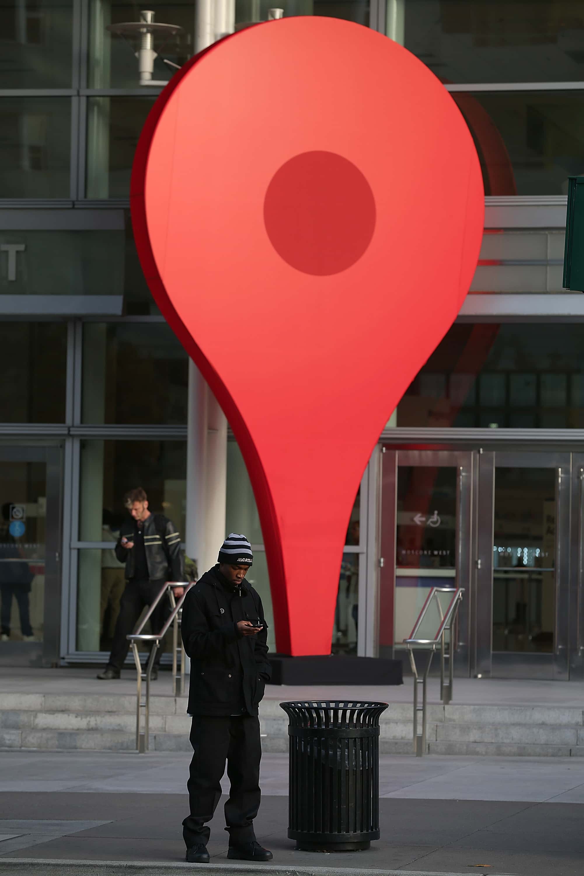A man stands next to an oversized Google map marker pin as attendees wait to enter the Google I/O developers conference at the Moscone Center on May 15, 2013 in San Francisco, California.  Thousands are expected to attend the 2013 Google I/O developers conference that runs through May 17.