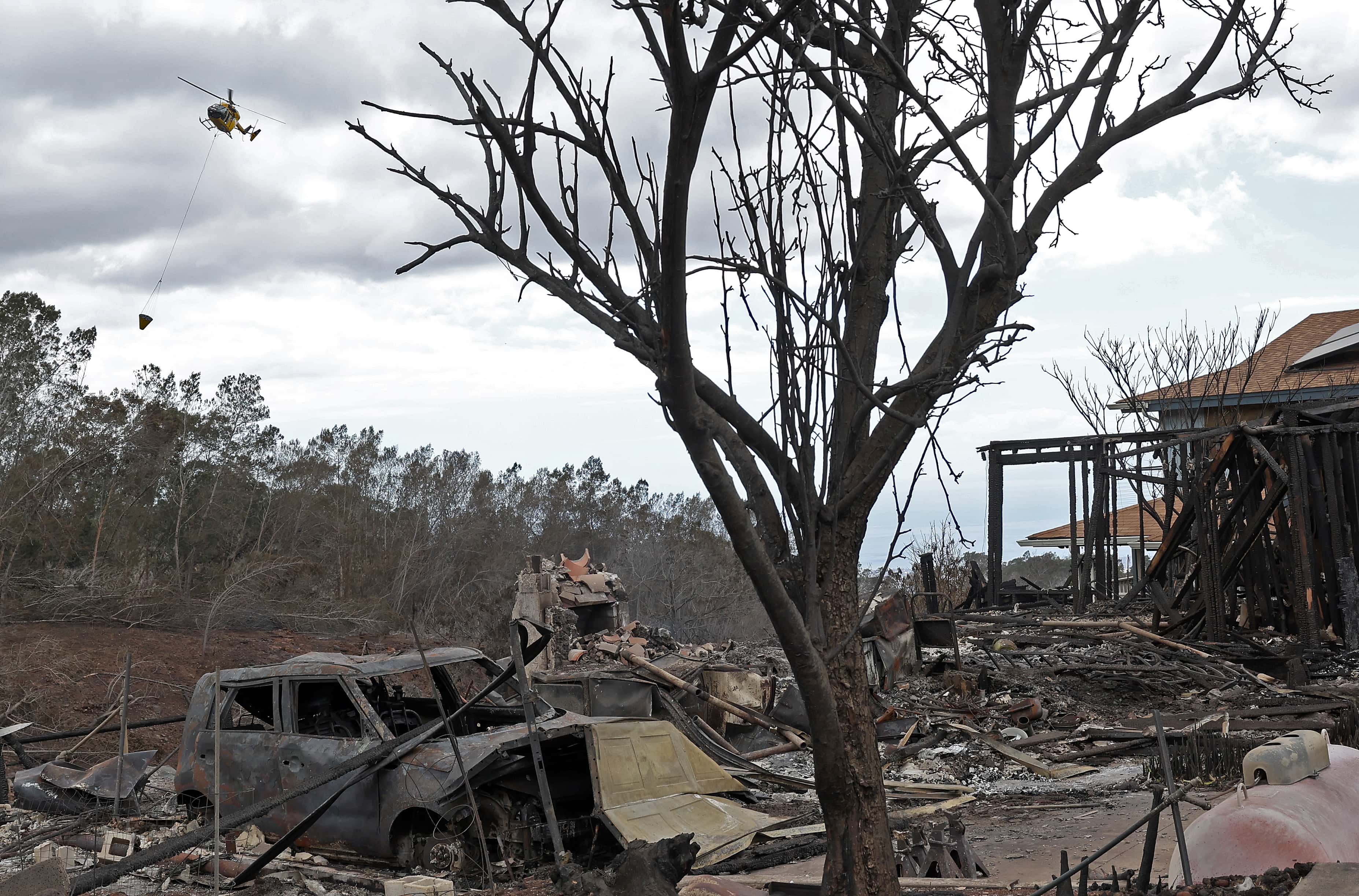 A firefighting helicopter prepares to drop water near a home that was destroyed by a wildfire on August 11, 2023, in Kula, Hawaii. (Photo by Justin Sullivan/Getty Images)