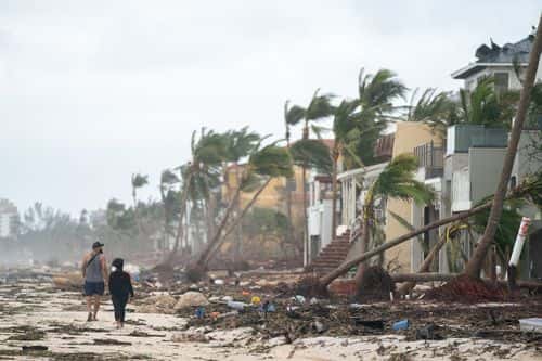 People walk along the beach looking at property damaged by Hurricane Ian on September 29, 2022 in Bonita Springs, Florida. The storm made a U.S. landfall on Cayo Costa, Florida, and brought high winds, storm surges, and rain to the area causing severe damage.