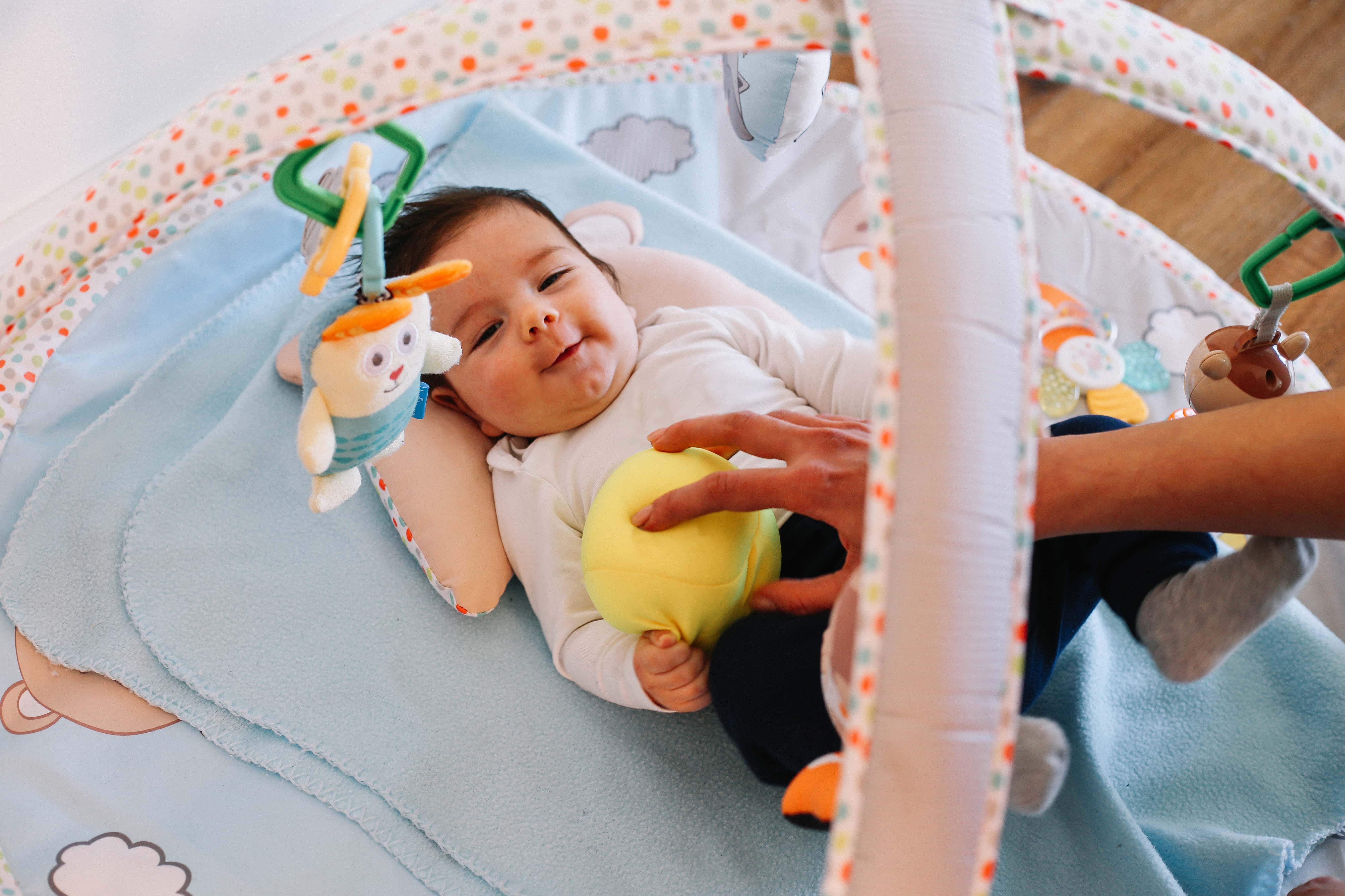 Smiling little baby boy playing with toys, enjoying being at home with mom.