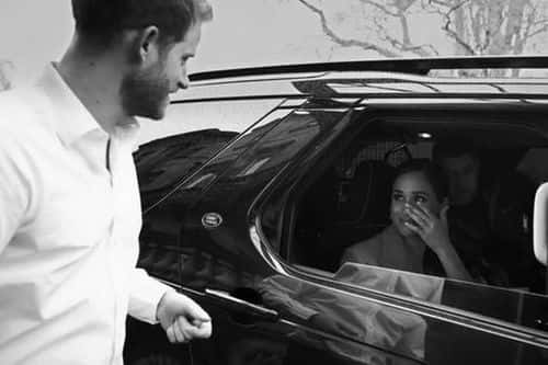 A black and white shot of Meghan crying in the back of a car as she gazes at Harry (Netflix)