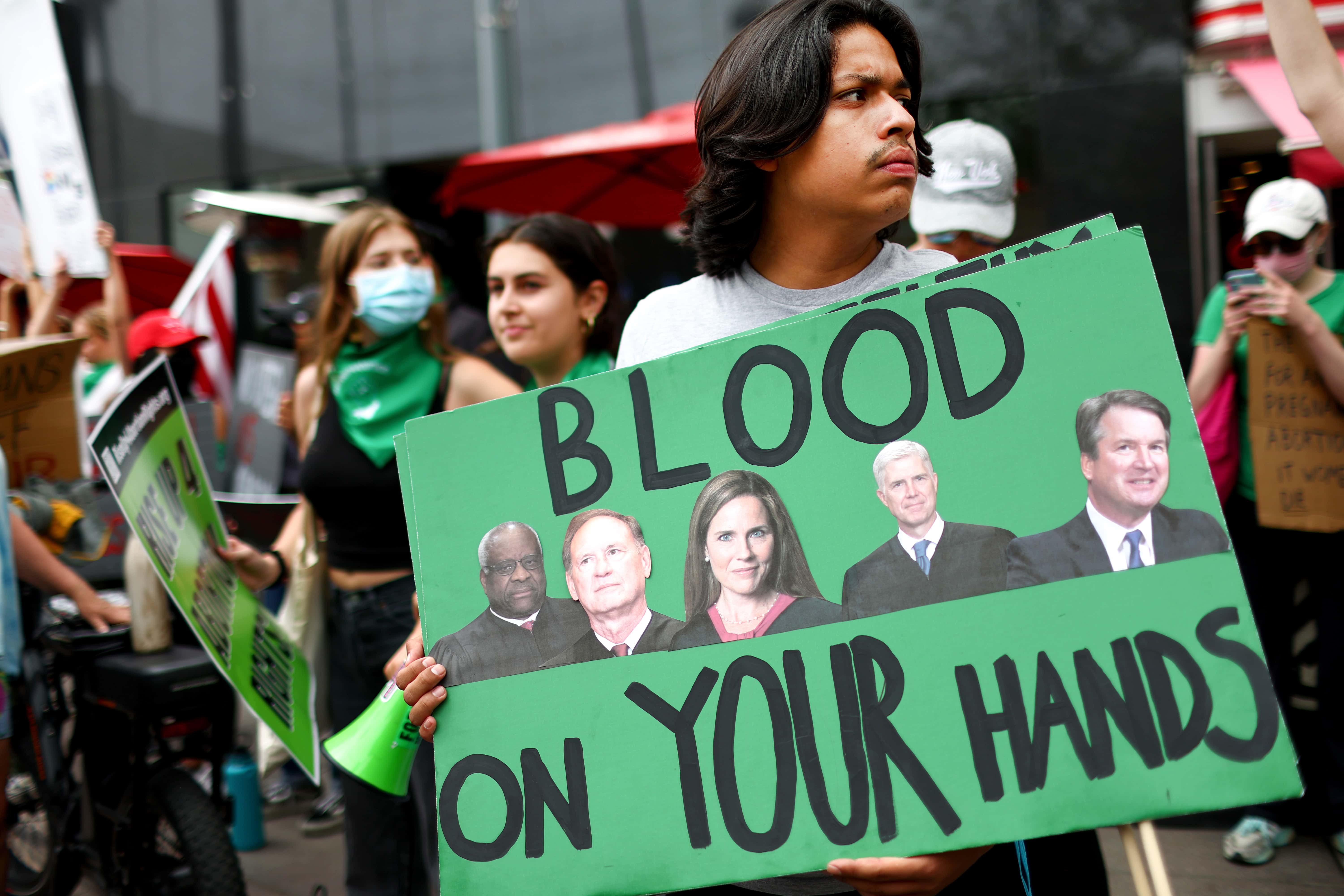 An abortion-rights activist holds a sign depicting Supreme Court Justices Clarence Thomas, Samuel A. Alito, Jr., Amy Coney Barrett, Neil M. Gorsuch, and Brett M. Kavanaugh during a demonstration outside a Planned Parenthood clinic as they safeguard the clinic from a possible protest by a far-right group on July 16, 2022 in Santa Monica, California. On July 9, a protest by far-rights groups outside the clinic forced it to shut down early. The Supreme Court's recent decision in Dobbs v Jackson Women's Health overturned the landmark 50-year-old Roe v Wade case and erased a federal right to an abortion. (Photo by Mario Tama/Getty Images)