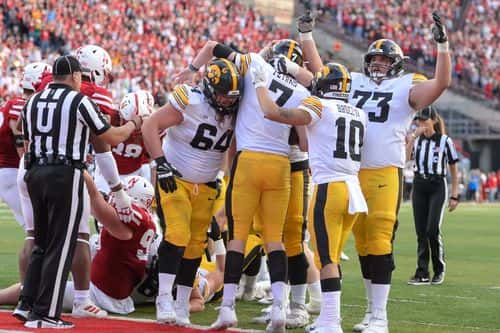 Quarterback Spencer Petras #7 of the Iowa Hawkeyes and offensive lineman Cody Ince #73 and wide receiver Arland Bruce IV #10 and offensive lineman Kyler Schott #64 celebrate scoring the winning touchdown against the Nebraska Cornhuskers in the second half at Memorial Stadium on November 26, 2021 in Lincoln, Nebraska.