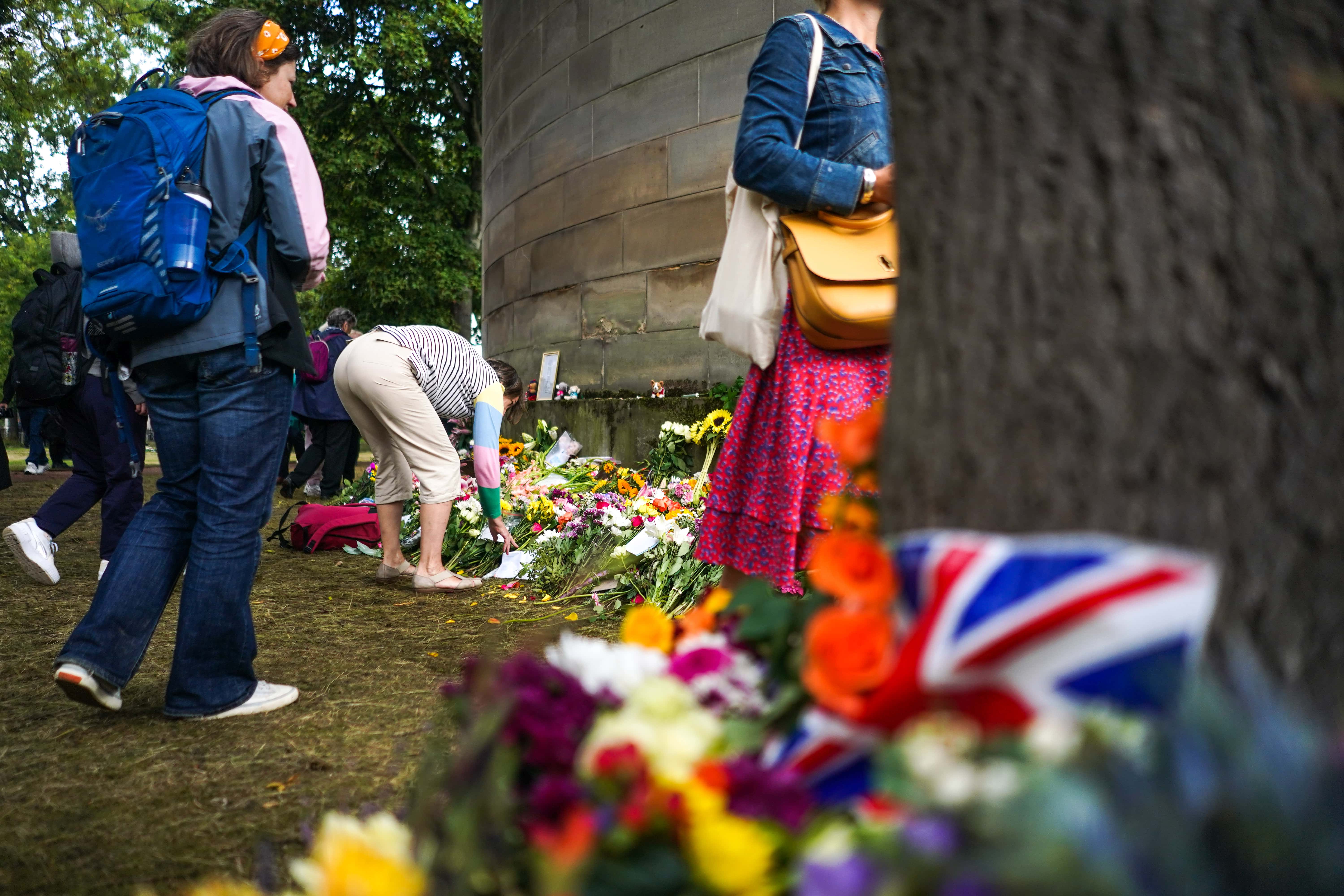 People view flowers which have been laid in remembrance of the late Queen Elizabeth II outside the Palace of Holyroodhouse on September 12, 2022 in Edinburgh, Scotland. King Charles III joins the procession accompanying Her Majesty The Queen's coffin from the Palace of Holyroodhouse along the Royal Mile to St Giles Cathedral. The King and The Queen Consort, accompanied by other Members of the Royal Family also attend a Service of Prayer and Reflection for the Life of The Queen where it lies in rest for 24 hours before being transferred by air to London. (Photo by Peter Summers/Getty Images)