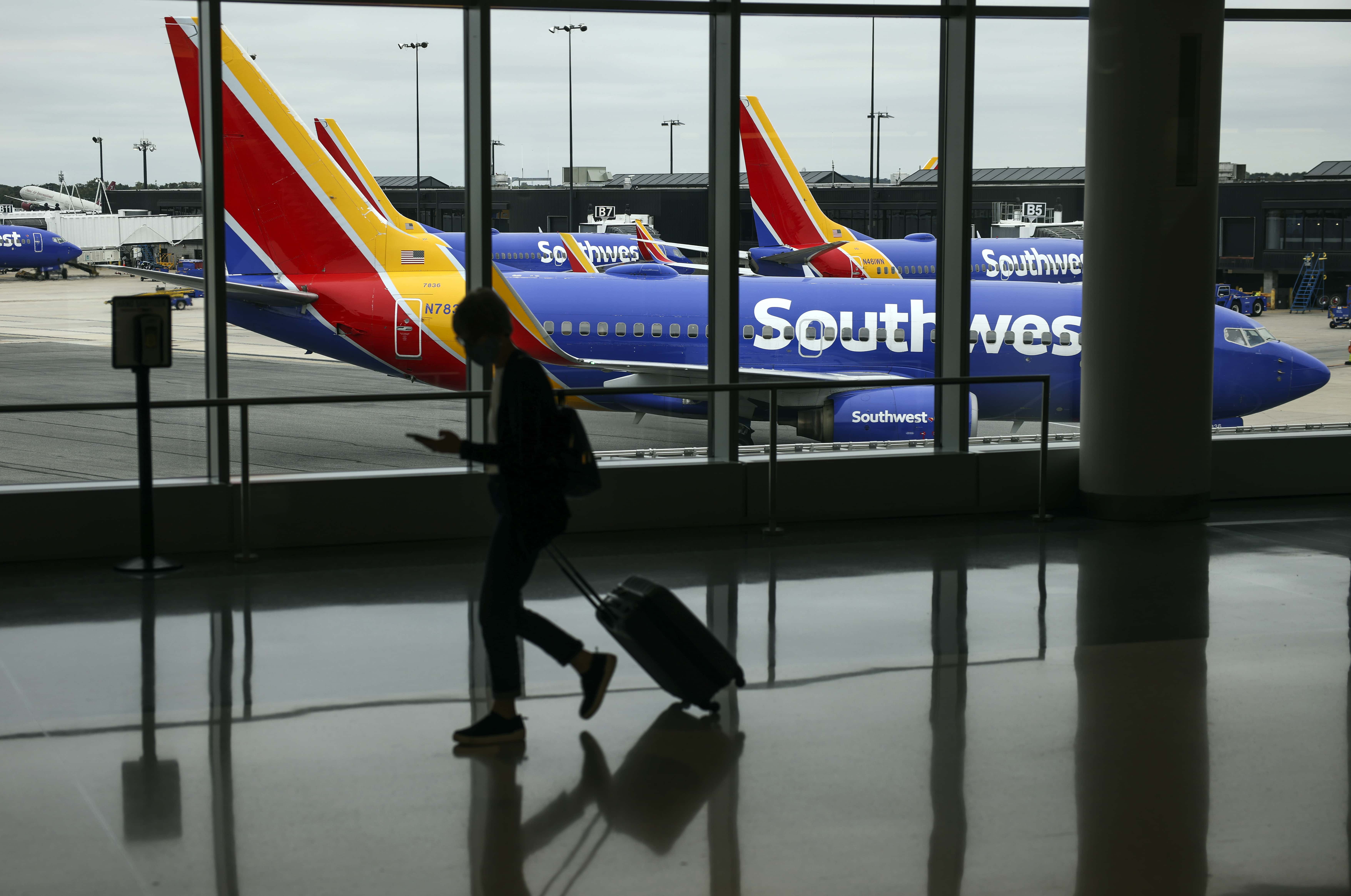 A traveler walks past a Southwest Airlines airplane as it taxies from a gate at Baltimore Washington International Thurgood Marshall Airport on October 11, 2021 in Baltimore, Maryland. Southwest Airlines is working to catch up on a backlog after canceling hundreds of flights over the weekend, blaming air traffic control issues and weather.
