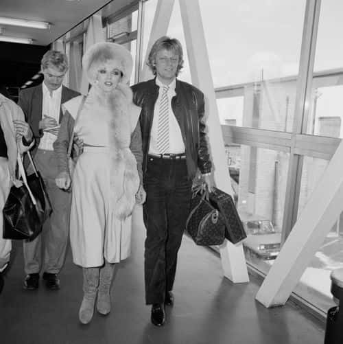 English actress Joan Collins at a London airport with her fiance, Swedish pop singer Peter Holm, 21st October 1984. (Photo by David Parker/Express/Getty Images)